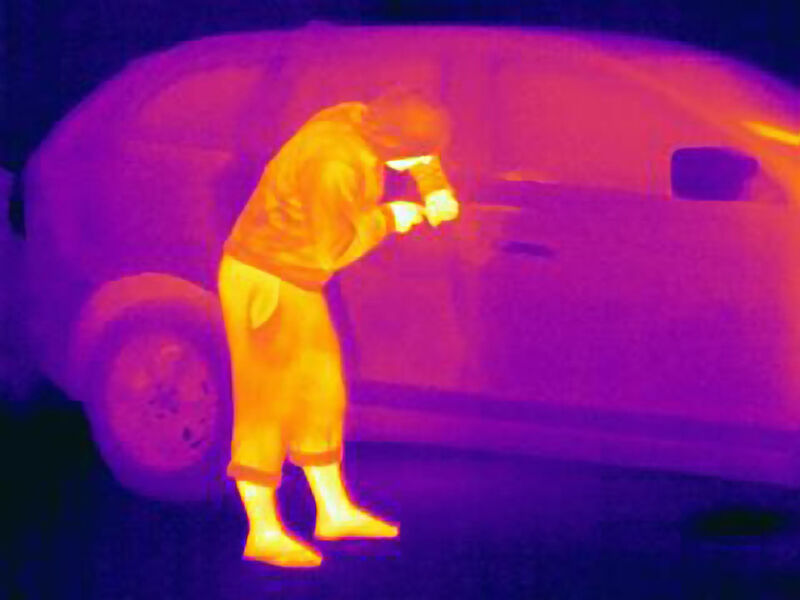 Infrared image of a person jimmying open a vehicle.