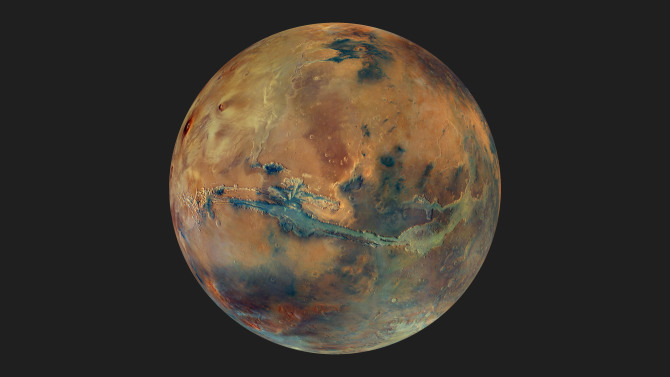 This image shows the globe of Mars set against a dark background. The disc of the planet features yellow, orange, blue and green patches, all with an overall muted grey hue, representing the varying composition of the surface.